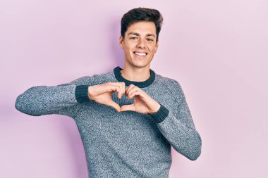 Gündelik kıyafetler giyen, aşık gülümseyen, elleriyle kalp sembolü yapan genç bir İspanyol. romantik kavram. 