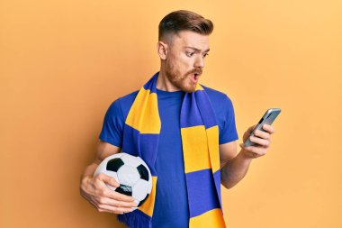 Genç kızıl saçlı adam holigan atkısı takıyor ve şok olmuş suratına akıllı telefon kullanıyor. Şüpheci ve alaycı görünüyor. 