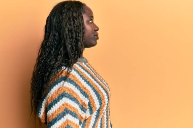 Yünlü kış kazağı giyen Afrikalı genç bir kadın, rahat bir görünüm ve kendine güvenen bir gülümsemeyle poz veriyor.. 