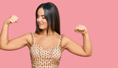 Seksi parti elbisesi giyen genç, güzel İspanyol kız kollarında gururla gülümseyen kaslar gösteriyor. fitness konsepti. 