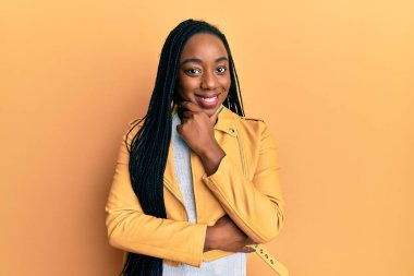 Young african american woman wearing casual jacket looking confident at the camera smiling with crossed arms and hand raised on chin. thinking positive. 