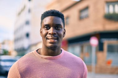 Genç Afrikalı Amerikalı adam gülümseyerek şehirde mutlu mesut duruyor..