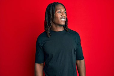 Saçları örgülü Afro-Amerikalı bir adam rahat bir görünüm takınıyor doğal bir yüzü ve kendine güvenen bir gülümsemesi var.. 