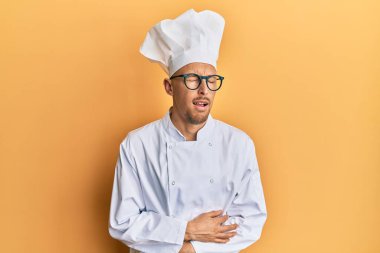 Bald man with beard wearing professional cook uniform with hand on stomach because nausea, painful disease feeling unwell. ache concept. 