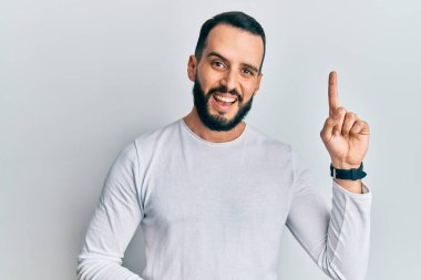 Sakallı, sıradan beyaz gömlekli genç bir adam bir fikir ya da soruyla gülümsüyor ve mutlu bir yüzle işaret ediyor. 