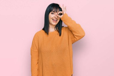 Gündelik kıyafetler giyen genç İspanyol kadın el hareketleriyle gülümsüyor ve mutlu yüzüyle parmaklarının arasından bakıyor.. 