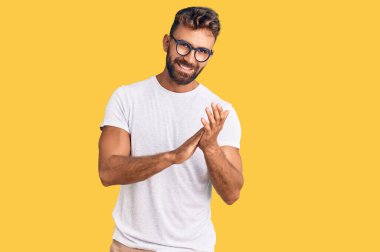 Latin asıllı genç adam, günlük kıyafetler ve gözlükler takıp alkışlıyor ve mutlu, neşeli ve gururlu elleri alkışlıyor. 