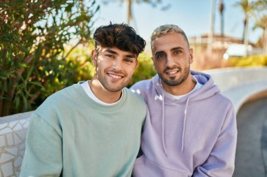 Genç eşcinsel çift gülümsüyor, şehirde bankta otururken mutlu..