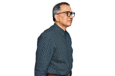 Orta yaşlı Hintli bir adam günlük giysiler ve gözlük takıyor. Taraf arıyor, rahat profil pozu veriyor. Kendine güvenen bir gülümsemesi var.. 