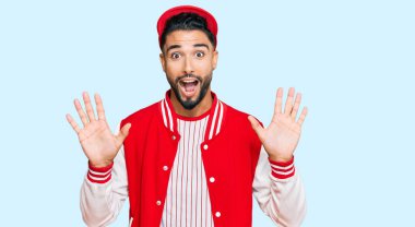 Young man with beard wearing baseball uniform celebrating crazy and amazed for success with arms raised and open eyes screaming excited. winner concept 