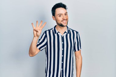 İspanyol asıllı genç adam, gündelik giysiler giyip dört numarayı gösterip işaret ederken kendinden emin ve mutlu bir şekilde gülümsüyor.. 