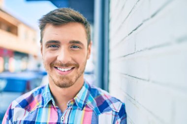 Beyaz bir adam gülümsüyor. Şehrin duvarına yaslanıyor..