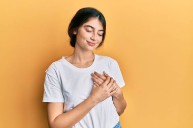 Beyaz bir tişört giyen, göğsünde elleri kapalı, yüzünde minnet dolu bir jest olan beyaz bir kadın. sağlık kavramı. 