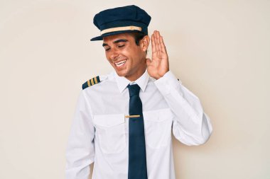 Uçak pilotu üniforması giyen, ağzı kulaklarında gülümseyen genç İspanyol bir adam dedikoduları ve dedikoduları dinliyor. Sağırlık kavramı. 