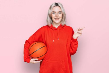Basketbol topunu tutan genç sarışın kız gülümsüyor. 