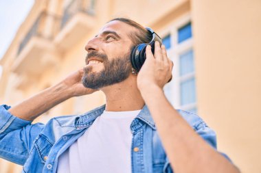 Orta Doğulu genç adam şehirde kulaklık takarak mutlu bir şekilde gülümsüyor..