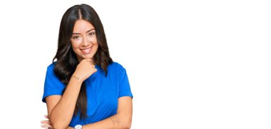 Güzel esmer, gündelik kıyafetler giyen genç bir kadın kameraya kendinden emin bir şekilde bakıyor kollarını kavuşturmuş ve çenesini kaldırmış gülümsüyor. Olumlu düşünmek. 