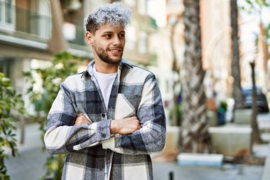 Genç İspanyol adam mutlu bir şekilde gülümsüyor şehirde çapraz hareketlerle.