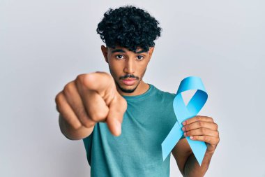 Genç Arap yakışıklı adam elinde mavi kurdeleyle kamerayı işaret ediyor ve sen kendine güvenen, ciddi görünüyorsun. 