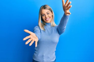 Güzel sarışın kadın sıradan kıyafetler giyip kameraya bakıyor. Sarılmak için kollarını açmış gülümsüyor. Mutluluğu kucaklayan neşeli bir ifade.. 