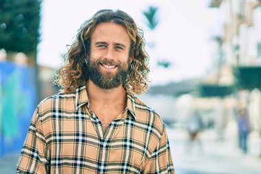 Uzun saçlı beyaz bir adam şehirde mutlu bir şekilde gülümsüyor..