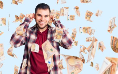 Gündelik tişört giyen genç yakışıklı adam gülümseyerek kulaklarını parmaklarıyla çekiyor, komik bir jest. deneme sorunu