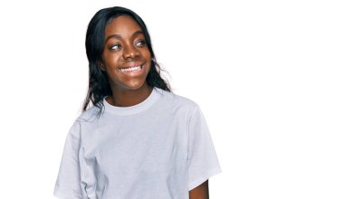 Gündelik beyaz tişört giyen genç Afro-Amerikan kadın yüzünde gülümseme, doğal bir ifade ile yan yana bakıyor. Kendinden emin gülen. 