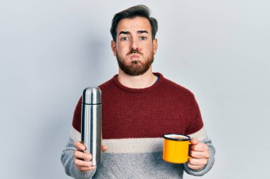 Sakallı, bir fincan kahve içen, termo şişiren komik suratlı yakışıklı beyaz adam. Ağzı havayla şişer, havayı yakalar.. 