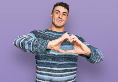 Gündelik kıyafetler giyen, aşık gülümseyen, elleriyle kalp sembolü yapan İspanyol genç bir adam. romantik kavram. 