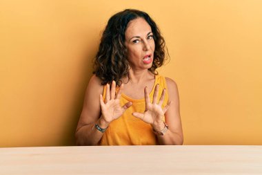 Masaya oturmuş sıradan kıyafetler giyen güzel orta yaşlı bir kadın avuç içlerini hareket ettiriyor. Korkmuş ve iğrenç bir ifadeyle reddediyor. Dur ve yasakla. 