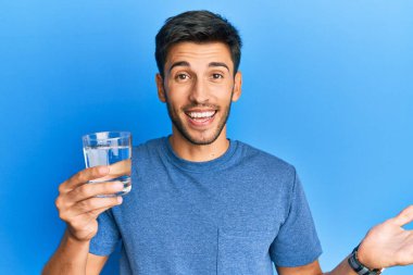 Genç yakışıklı adam bir bardak su içerek başarıyı mutlu bir gülümsemeyle ve kazanan yüz ifadesiyle kutluyor. 