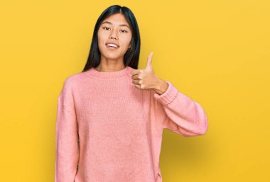 Güzel, genç Asyalı kadın sıradan bir kazak giyiyor ve elleriyle mutlu bir jest yapıyor. Kameraya bakıp başarıyı gösteren ifade. 