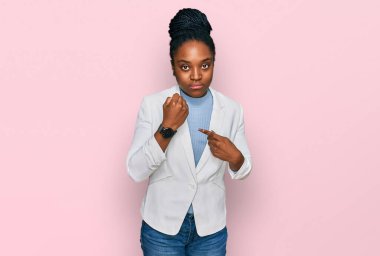 Genç Afro-Amerikan kadın iş kıyafetleri giyiyor. Aceleyle saati, sabırsızlığı ve rahat bir ifadeyle kameraya bakıyor. 