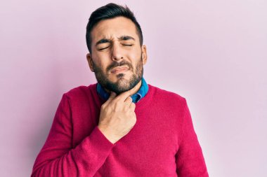 Günlük giysiler giyen genç İspanyol adam ağrılı boyuna dokunuyor, grip, mantar ve enfeksiyon yüzünden boğaz ağrısı çekiyor. 