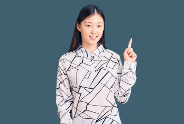 Gündelik tişört giyen genç, güzel Çinli bir kadın başarılı bir fikri işaret ediyor. Heyecanlı ve mutlu. Bir numara.. 