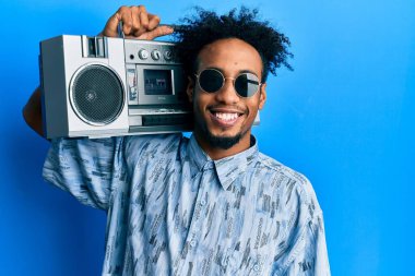 Young african american man with beard holding boombox, listening to music looking positive and happy standing and smiling with a confident smile showing teeth 