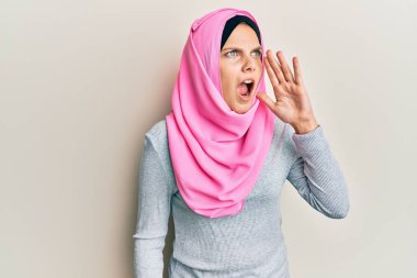 Geleneksel İslami başörtüsü takan genç beyaz kadın bağırıyor ve ağızdan ağıza bağırıyor. iletişim konsepti. 