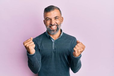 Orta yaşlı, sıradan kıyafetler giyen, mutlu ve heyecanlı bir adam kolları havada, gülümseyen ve başarı için bağıran, kazanan bir jest yapıyor. kutlama konsepti. 