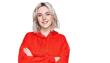 Sıradan kıyafetler giyen, kollarını kavuşturup kameraya bakan mutlu yüzlü genç sarışın kız. pozitif kişi. 