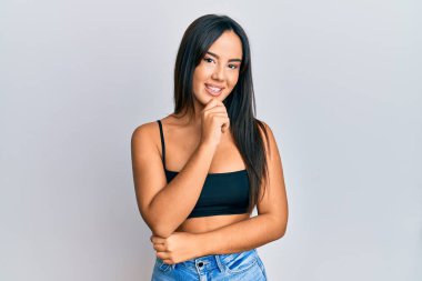 Gündelik giysiler giyen genç, İspanyol bir kız kameraya kollarını kavuşturup, çenesine dokunarak gülümsüyor. Olumlu düşünmek. 