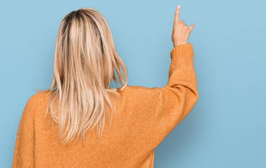 Middle age caucasian woman wearing casual winter sweater posing backwards pointing ahead with finger hand 