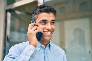 Genç Latin adam gülümsüyor ve şehirde akıllı telefondan konuşuyor..