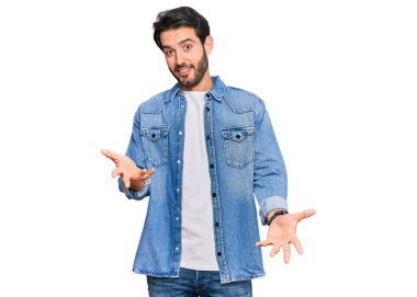 Gündelik kıyafetler giyen genç İspanyol adam güler yüzlü, kolları açık, dostça karşılama, olumlu ve kendinden emin selamlar. 