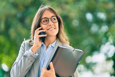 Genç İspanyol iş kadını gülümsüyor. Şehirdeki akıllı telefondan mutlu bir şekilde konuşuyor..