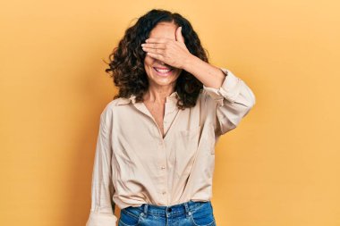 Orta yaşlı İspanyol kadın, sıradan kıyafetler giyiyor, gülümsüyor ve yüz yüze gülüyor. Şaşırtmak için gözleri örtüyor. kör kavram. 