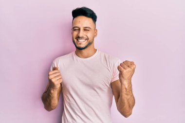 Gündelik giysiler giyen genç Arap adam başarı için heyecanlanıyor kolları havada ve gözleri kapalı zaferi kutluyor. Kazanan konsept. 