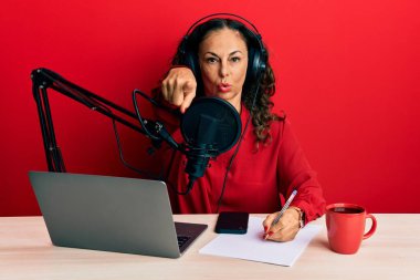 Radyo stüdyosunda çalışan orta yaşlı güzel bir kadın kamerayı işaret ediyor ve sen kendine güvenen ciddi bir hareket yapıyorsun. 