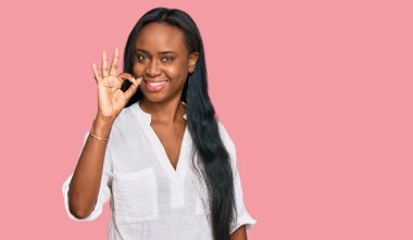 Gündelik kıyafetler giyen genç siyahi kadın pozitif gülümsüyor ve el ve parmaklarıyla 