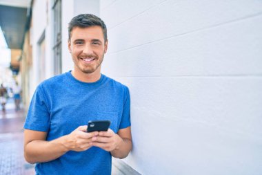 Beyaz adam şehirde akıllı telefon kullanarak mutlu bir şekilde gülümsüyor..