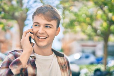 Genç beyaz adam gülümsüyor. Şehirdeki akıllı telefondan konuşuyor..